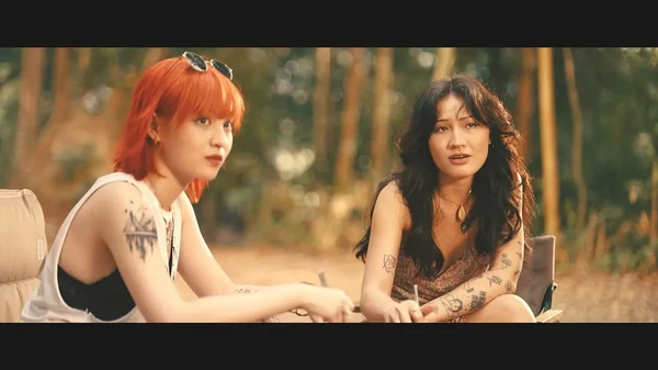 In the movie Móng Vuốt, two tattooed characters are engaged in a conversation in a forest setting.