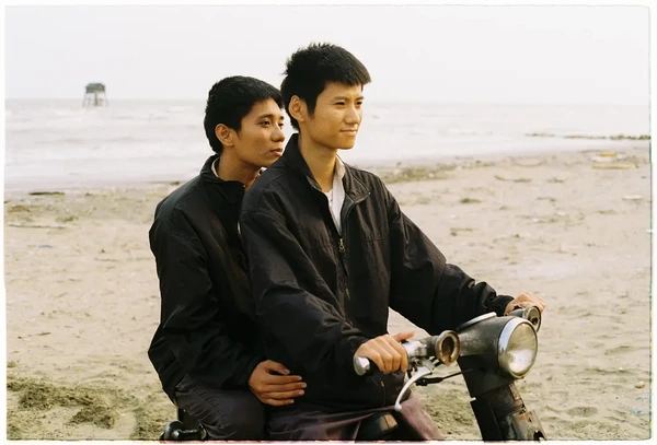 Two men riding a motorcycle on the beach in "Viet and Nam"