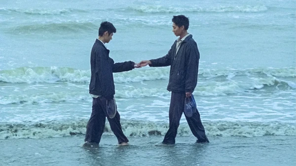 Two men exchanging something by the seashore in "Viet and Nam".