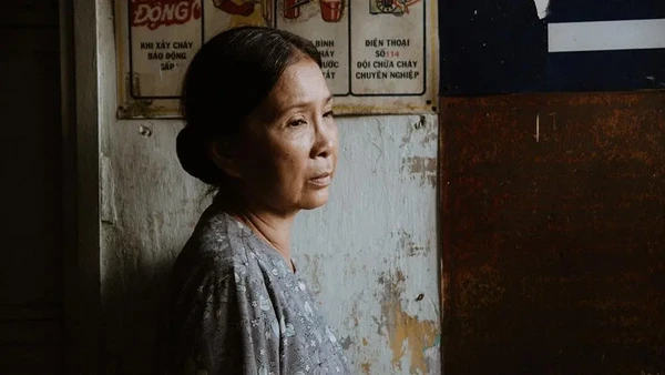 A woman stands pensively by a wall in "Có căn nhà nằm nghe nắng mưa".